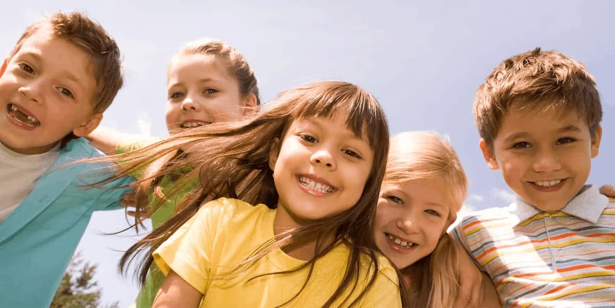 Five smiling primary school children huddled together outdoors under a blue sky