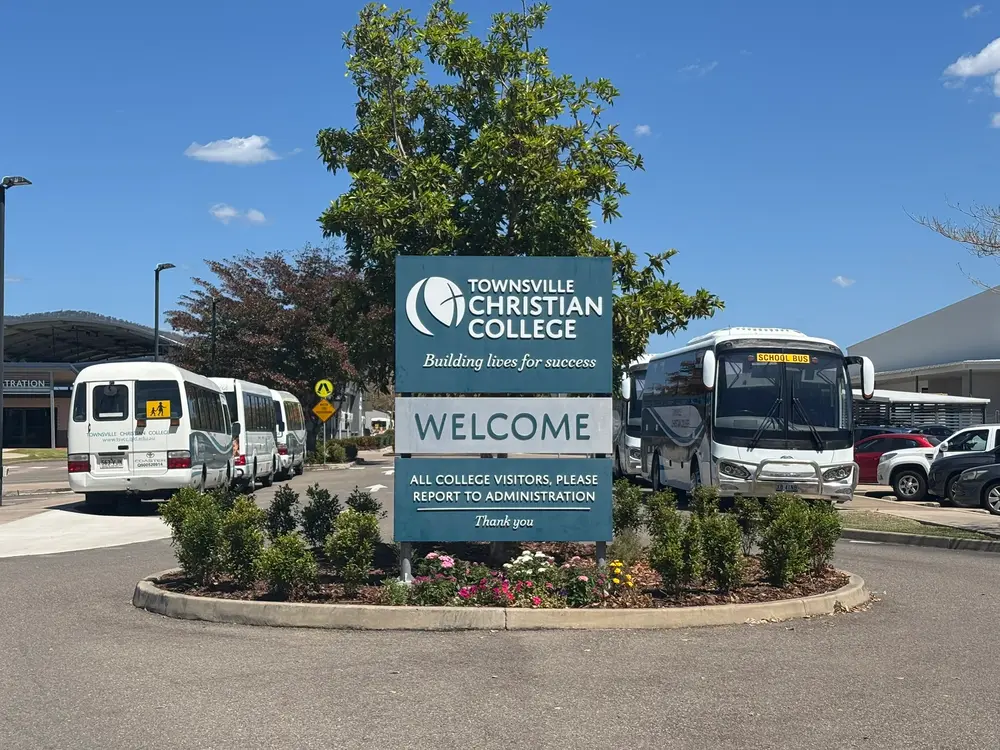 The welcome sign at Townsville Christian College, with the college's school buses parked behind it.